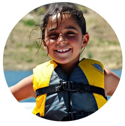 Girl wearing a lifevest sitting on a boat at summer camp and smiling.