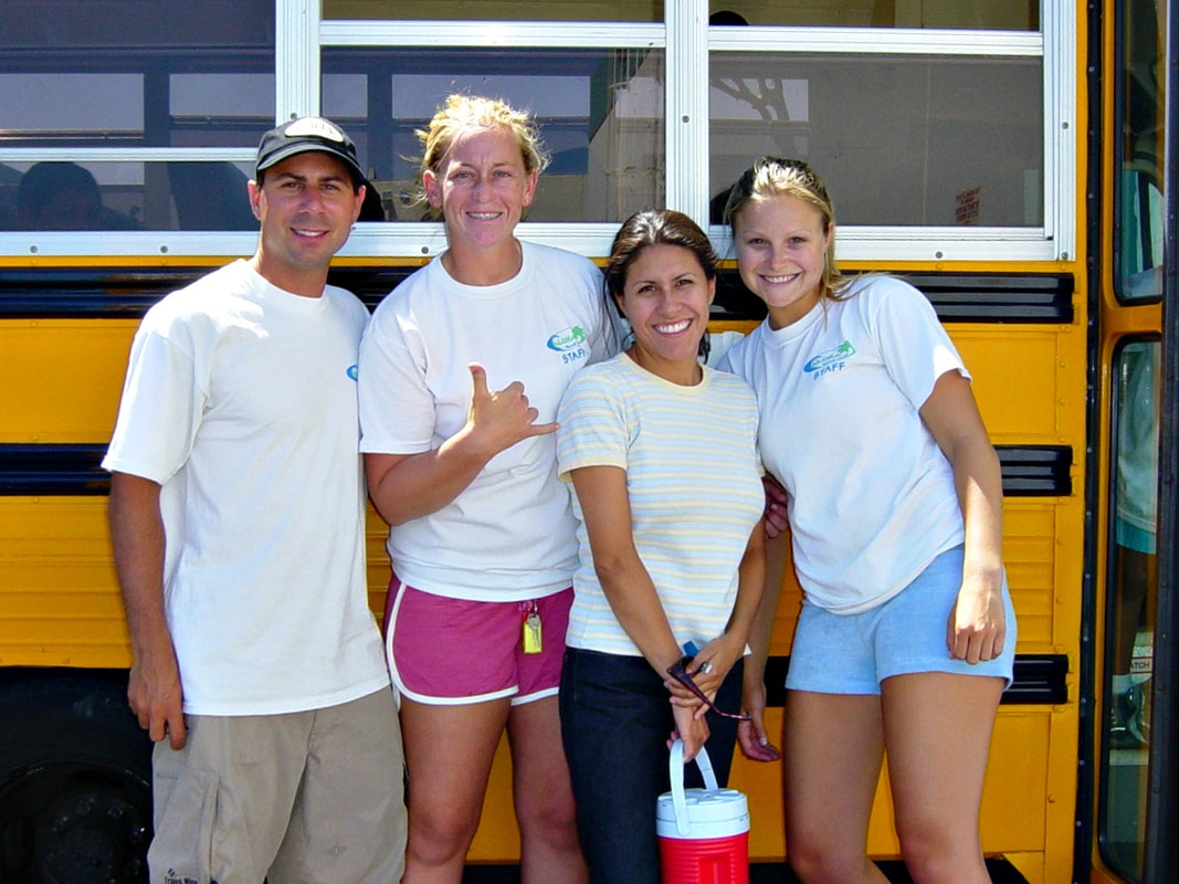 Four camp counselors standing in front of a summer camp bus