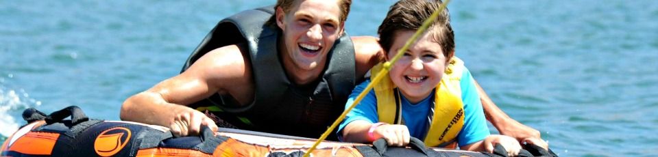 Male camp counselor and tween boy riding an innertube together and laughing at summer camp