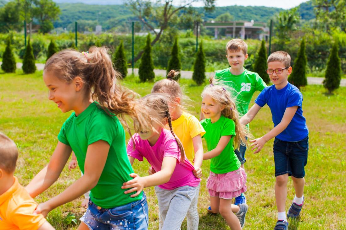 Group of 10 boys and girls playing together at summer camp on an outdoor grass field
