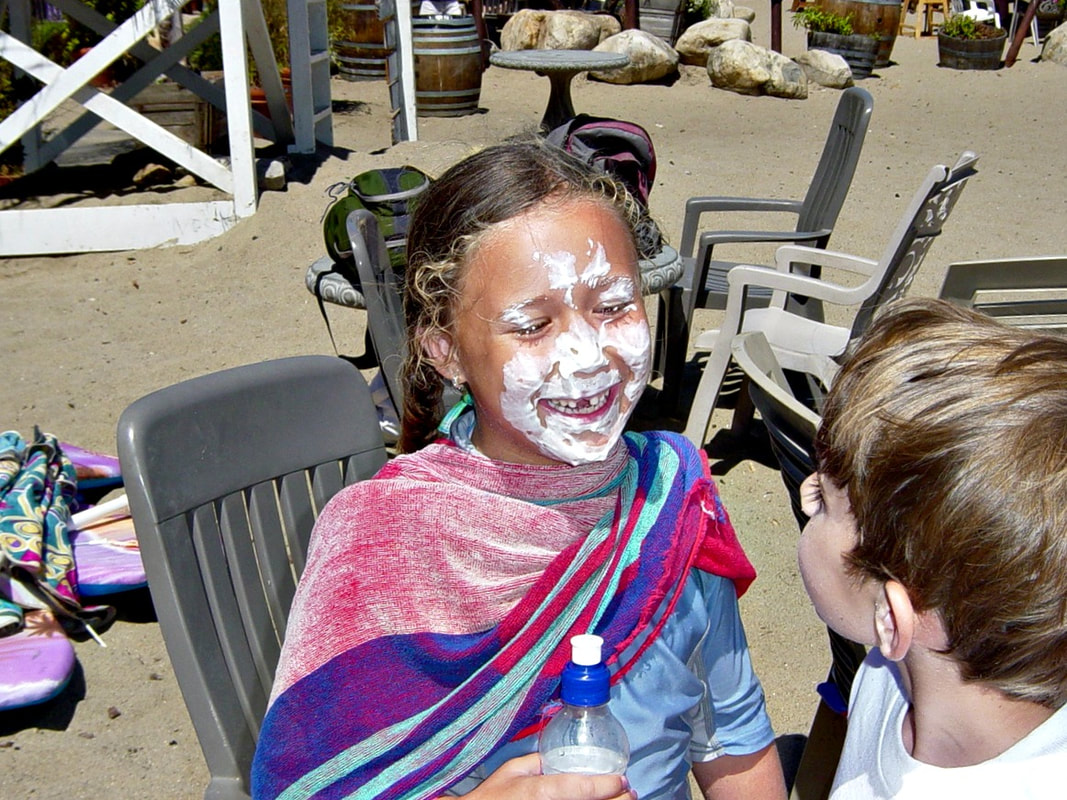 Happy girl at summer camp getting her face painted by another camper.