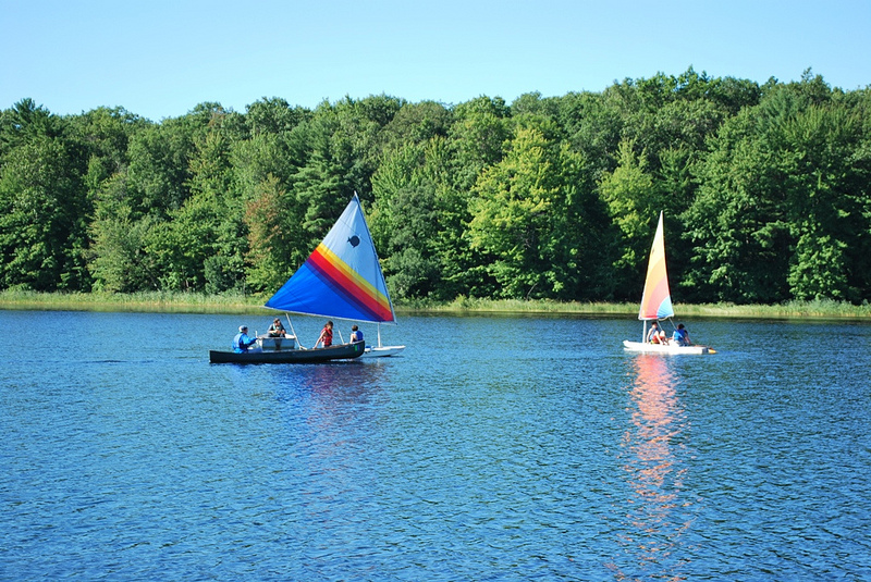 Campers sailing on sailboats on the lake at summer camp.