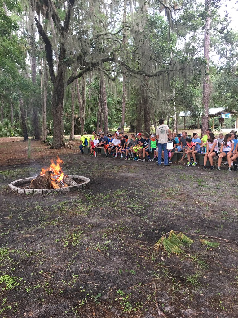 campers signing songs around the campfire as their camp counselor plays the guitar at summer camp.