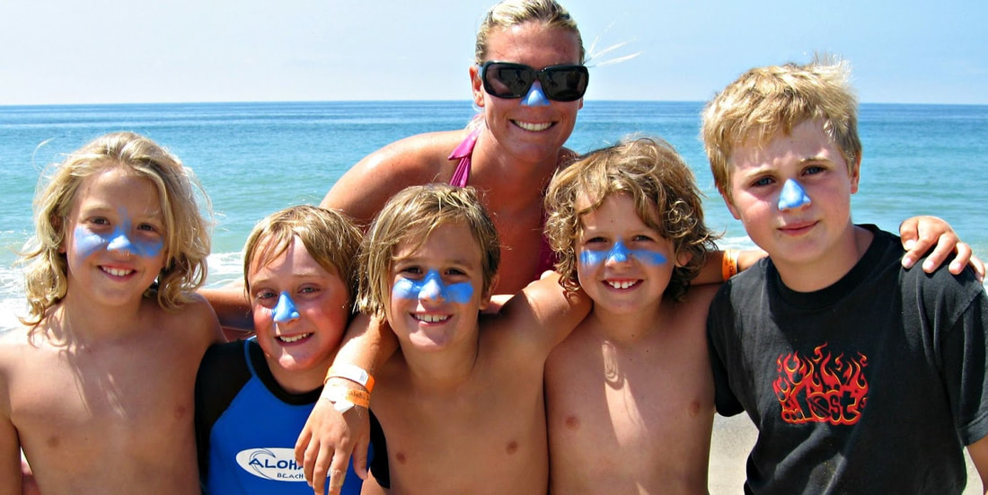 Five Aloha Beach Camp boys and their camp counselor standing in front of the ocean and wearing matching blue zynca sunscreen on their noses.
