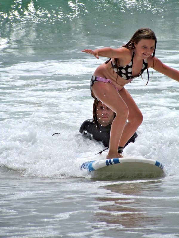 Girl surfing as her surf instructor looks on at Ballona Beach Summer Camp in Los Angeles