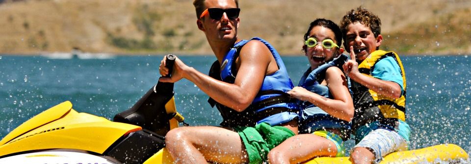 Camp counselor driving two campers on the back of his jet ski at summer camp