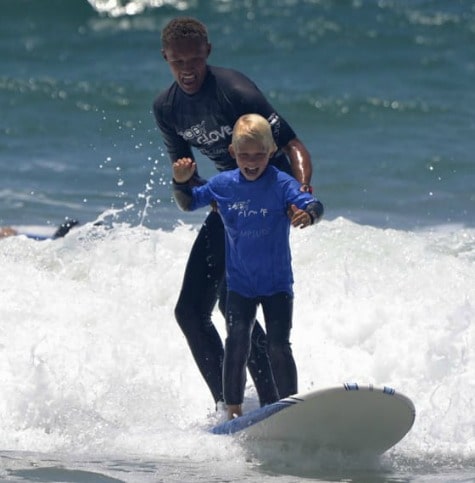 Boy learning to surf with the help and support of his surf camp instructor at Camp Surf.