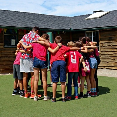 Campers and their counselor at Camp Ocean Pines huddling together in front of a cabin.