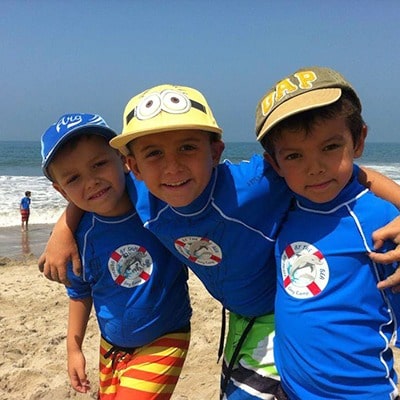 Three boys in Fitness by the Sea rash guards on the beach.