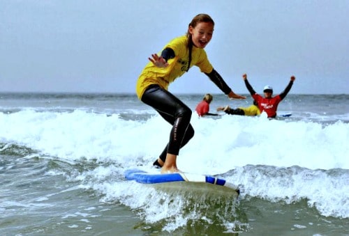 Camper surfing with her surf instructor in the back.