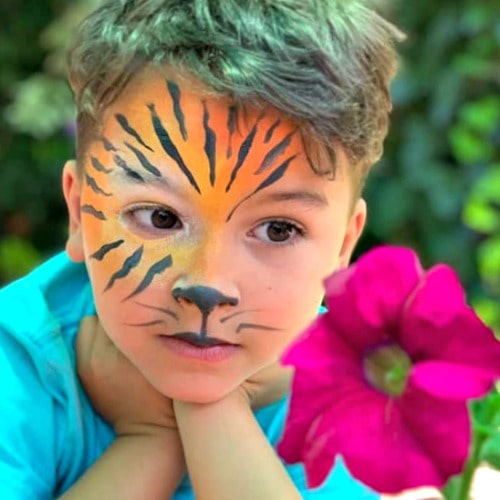 boy wearing black and yellow stripe tiger facepaint while admiring a pink flower at Kallpachy Spanish Adventure Summer Camp