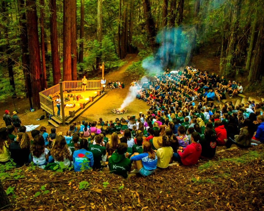 100's of campers and staff sitting around the campfire at Kennolyn Camps' overnight camp.