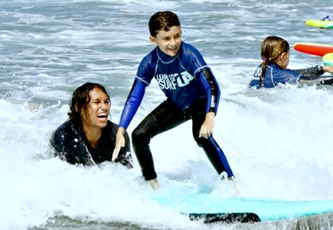 Boy surfing with his surf instructor in the back at Learn to Surf L.A.'s Los Angeles surf camp program.