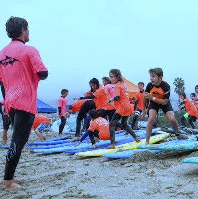 Group of campers standing on surfboards learning to surf on the sand at Malibu Makos Surf Camp.