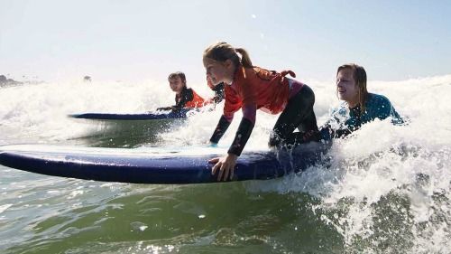 Female camper surfing in the ocean with support from her surf camp instructor at Malibu Makos surf camp.