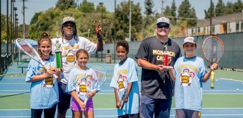 Campers and staff standing together on a tennis court holding tennis racquets.