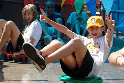 Camper sitting on a bench at Coach Steve's Summer of Fun Camp in L.A. giving the peace sign with both of her hands.