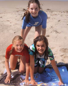 Three girls from Culver City forming a human pyramid on the beach and wearing summer camp rash guards at Aloha Beach Camp Summer Day Camp