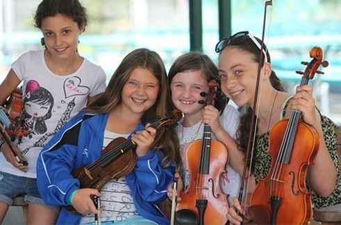 Four girls holding instruments and smiling at Santa Monica Music Camp.