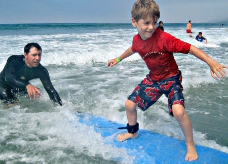Boy learning to surf at Aloha Beach Camp's Los Angeles surf camp program with the help of his camp counselor.