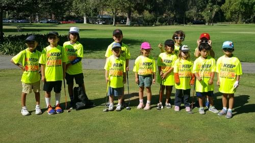 12 campers holding golf clubs and standing on the golf course in green TGA Premier Sports Camp t-shirts