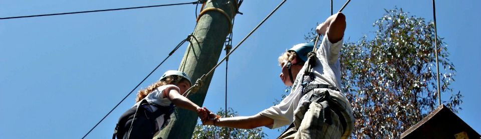 Two campers using teamwork to climb a ropes course together at Tumbleweed Day Camp in Los Angeles.