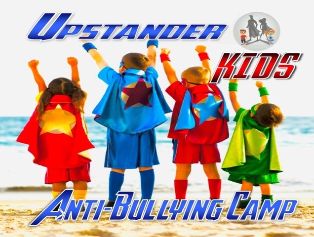 Four kids wearing superhero costumes standing on the beach facing the ocean with their arms up in the air, fists closed, in victory-type poses.